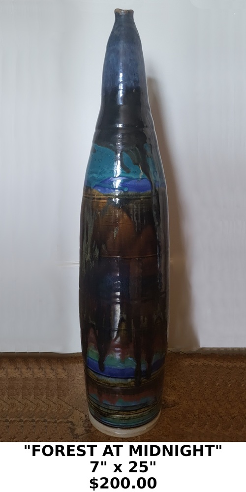 "FOREST AT MIDNNIGHT" 7" X 25" $200.00 This tall, slender ceramic vase is a fine example of studio art pottery. It features a characteristic drip glaze technique, where multiple colors—including deep blues, teals, and earthy browns—are layered and allowed to run down the surface during firing to create a dynamic, organic pattern. A tall "bottle" or "spindle" silhouette with a narrow neck, often used as a floor vase or a bold accent piece.