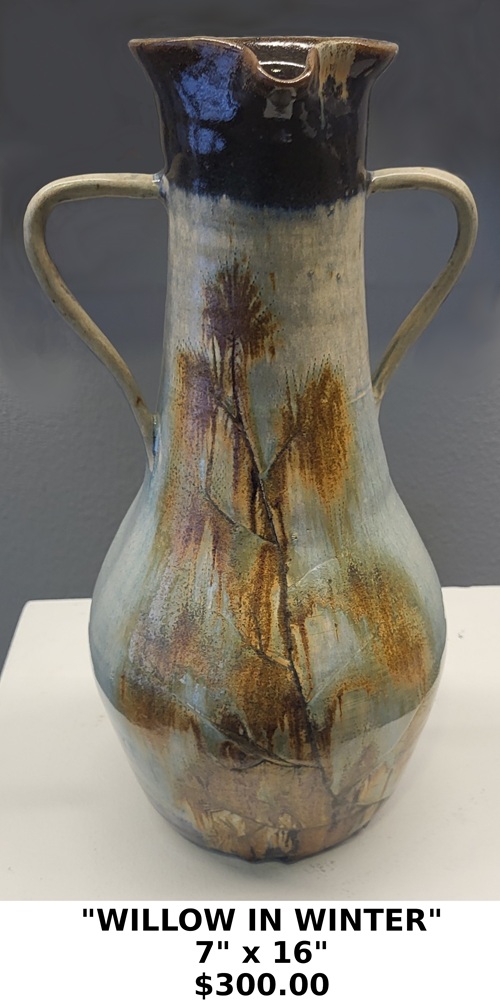 A tall, long-neck pitcher with two symmetrical handles and a wide, flared rim. The piece features a complex, multi-toned glaze with deep umber or dark brown at the rim, transitioning into cream, sand, and slate blue tones on the body. "WILLOW IN WINTER" 7" X 16" $300.00 The surface displays characteristic "droplet" effects and a granular texture often achieved through atmospheric firing (salt or wood firing).